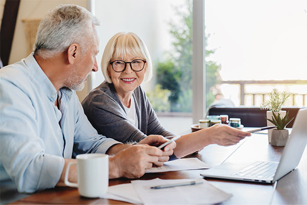 senior couple sitting at the kitchen counter looking at the laptop and having a happy conversation